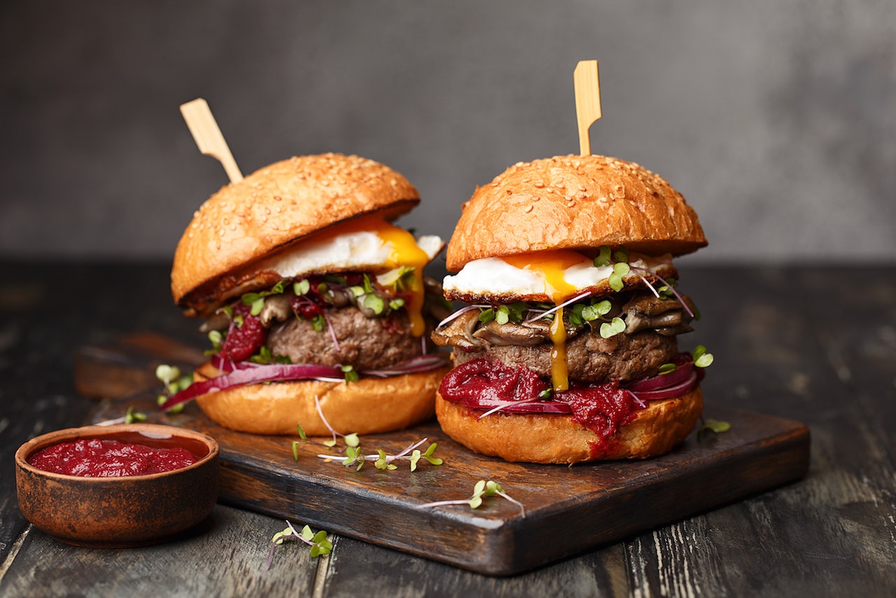 two beef burgers with egg and ketchup on the side