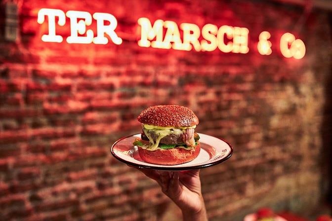 a burger on a plate and a neon sign of Ter Marsch & Co