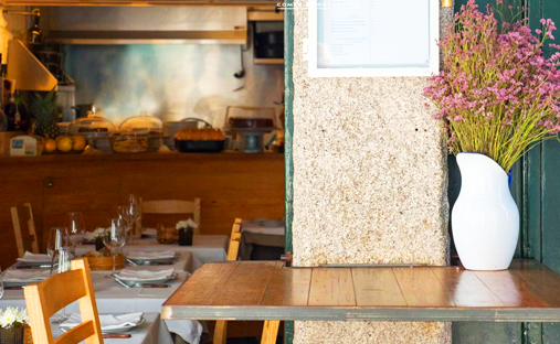 A vase with pink flowers on a table and the restaurant interior of Taberna dos Mercadores in the background