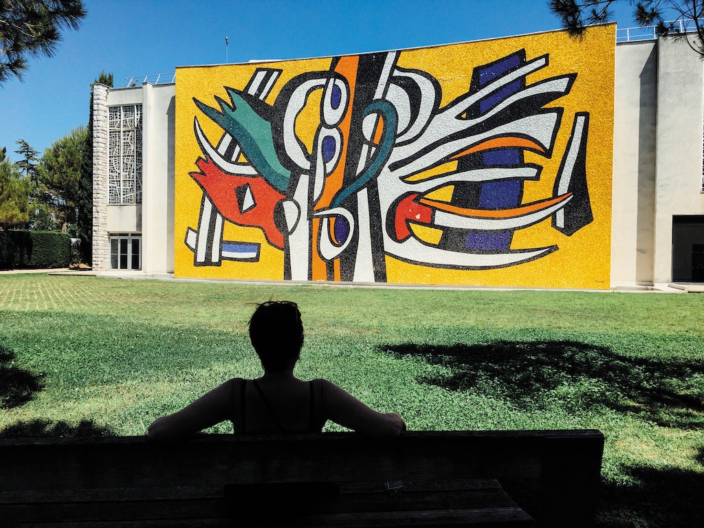 a woman sitting on a bench in front of the modernist exterior of the Musée Fernand Léger