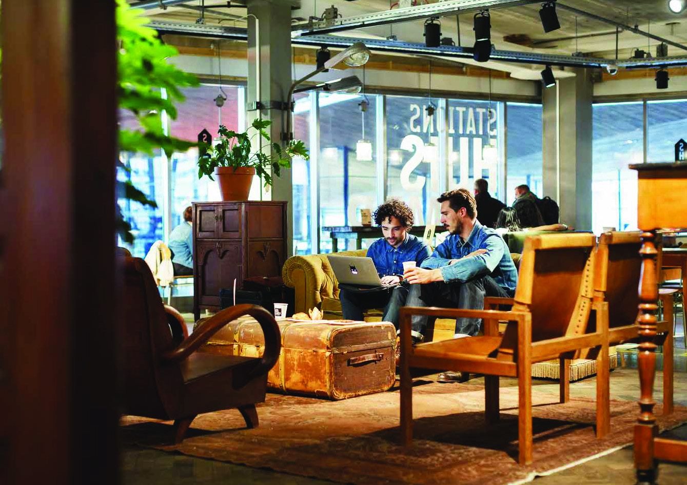 two men sitting inside of the StationsHuiskamer working on a laptop