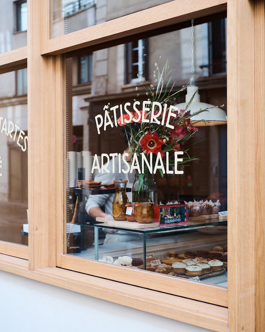 The window of Tapisserie with the words 'Pâtisserie Artisanale' painted on it and several small pastries on display.