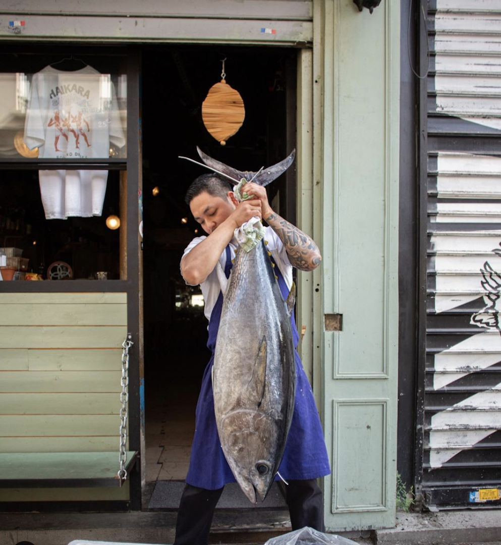 The chef at Haikara holds a big tuna fish by its tail in front of the restaurant in Paris