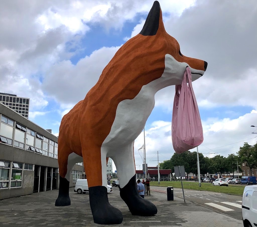 a giant-sized sculpture of a fox holding a shopping bag