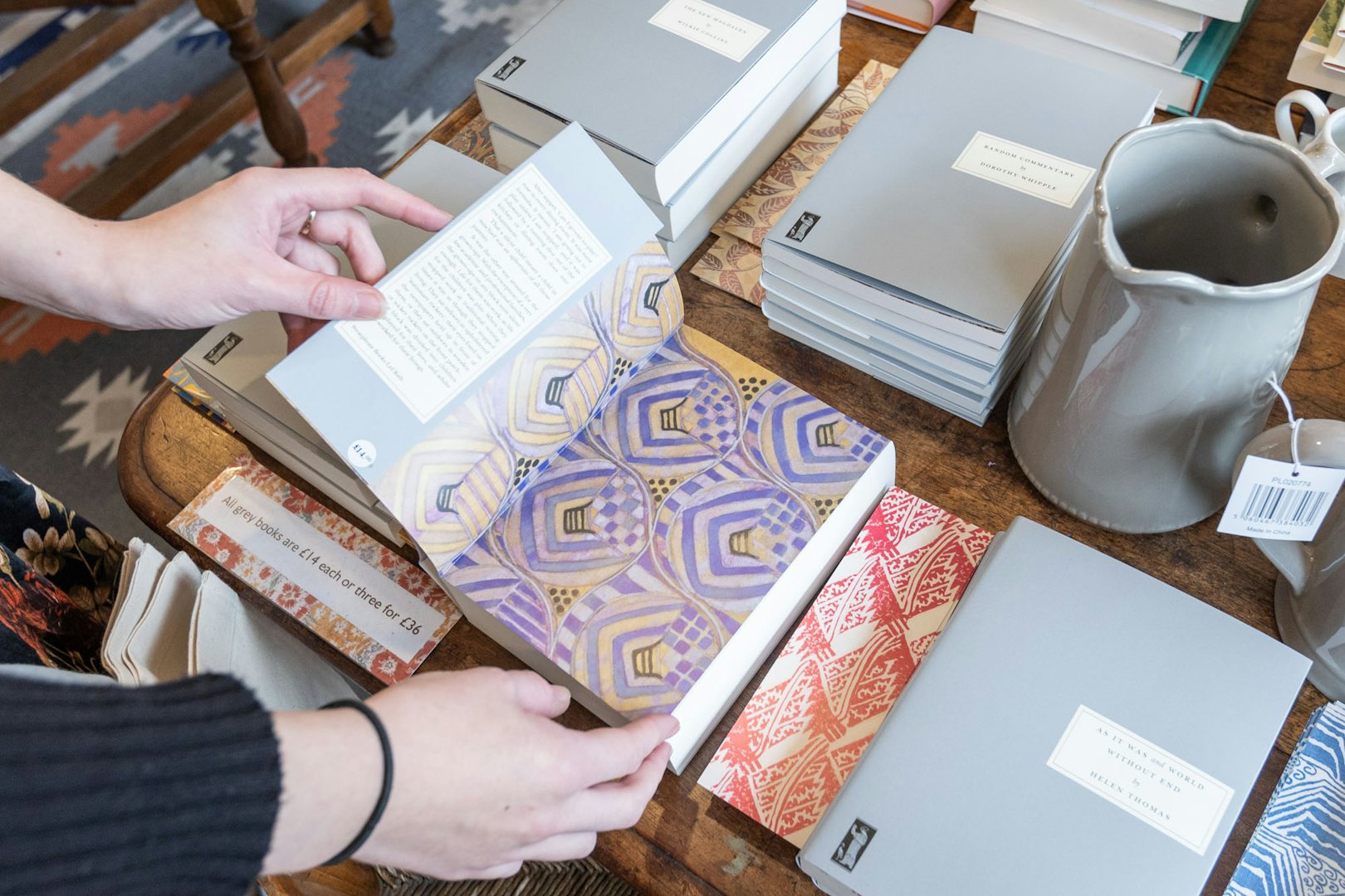 Hands holding a book open on a table at Persephone Books