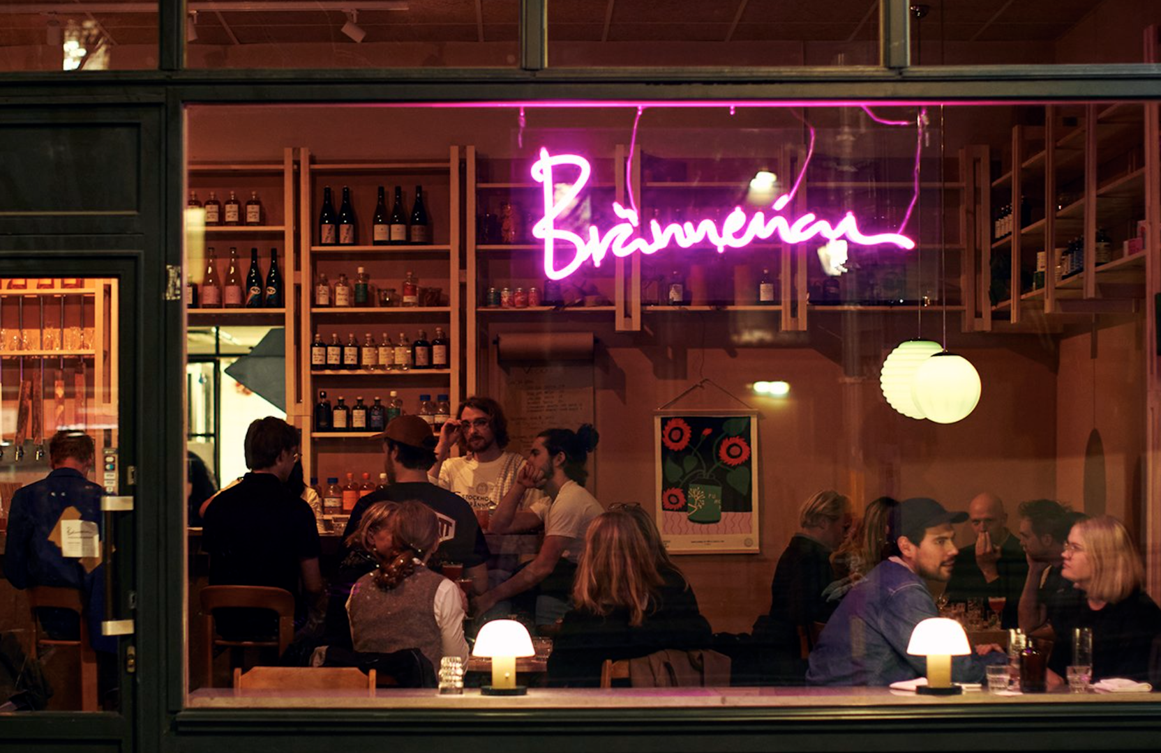 People drinking at Brännerian at night under a pink neon sign