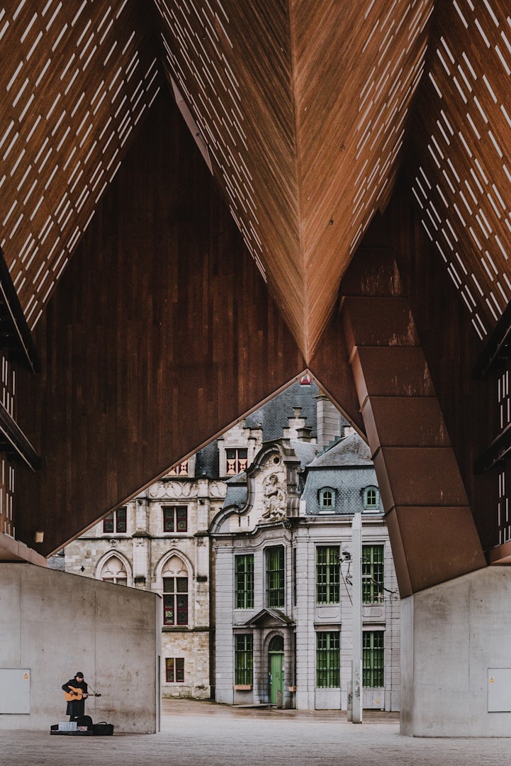 a man playing guitar under the striking Stadshal of Ghent