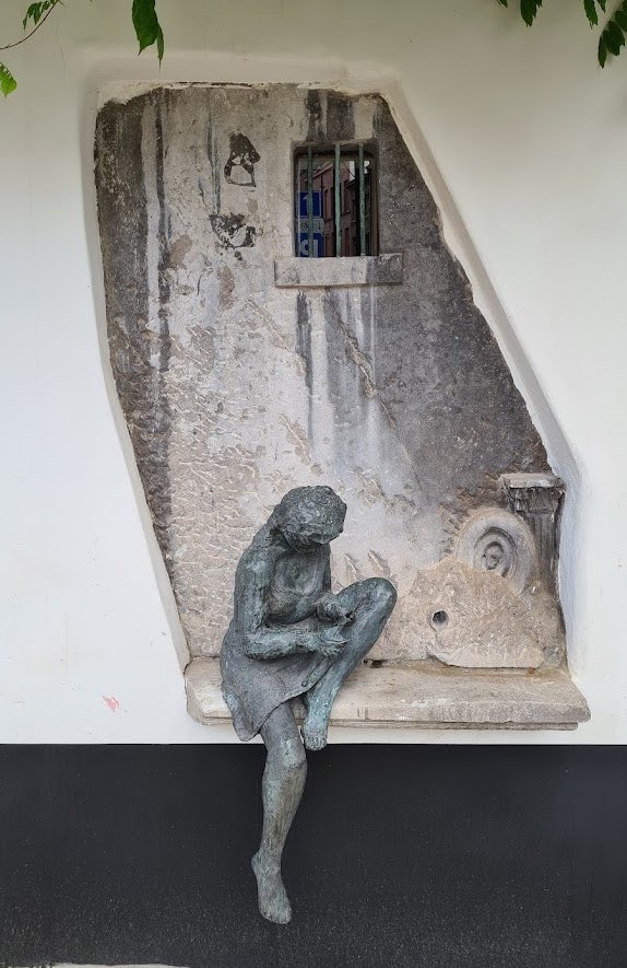 a statue of a little girl knitting by a wall in Ghent