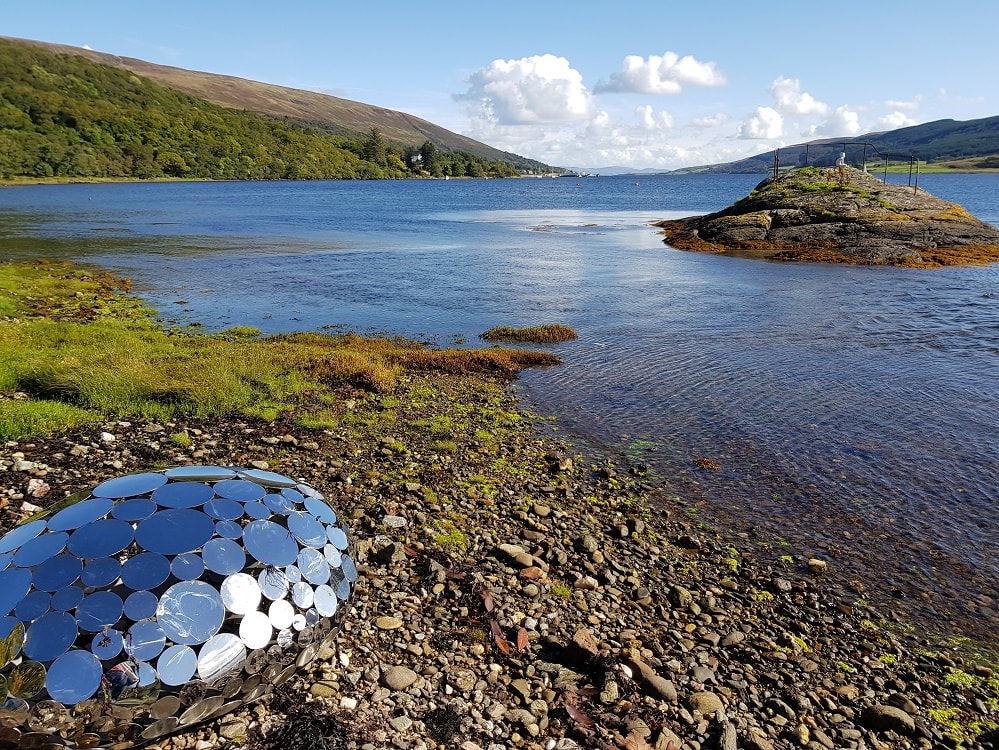 shiny metal sculpture by a lake at the Caol Ruadh Sculpture Park